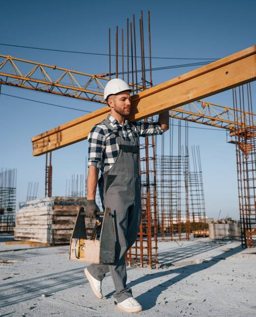 Holding big wooden piece. Man is working on the construction site at daytime.