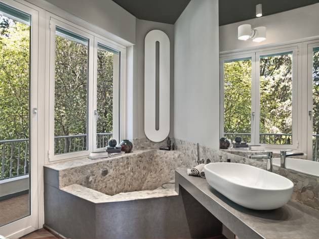 Interior view of a modern bathroom in the foreground the washbasin on the masonry top and in the corner on the background under the window there is the masonry bathtub