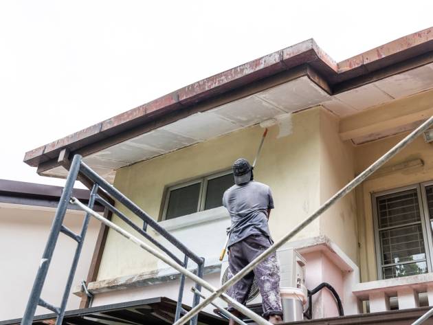 Painter worker adding undercoat foundation paint onto ceiling as primer with roller at residential building.